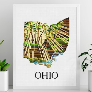 Pode incluir: Padrão de ponto cruz do estado de Ohio, com uma cena de floresta com árvores e um rio. A palavra "OHIO" é bordada abaixo do contorno do estado.
