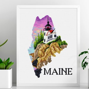 May include: Cross-stitch pattern of the state of Maine, featuring a lighthouse and a colorful sunset. The word "MAINE" is stitched below the image.