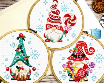 Può includere: Tre gnomi di Natale ricamati in cerchi bianchi. Lo gnomo a sinistra indossa un cappello verde con cuori e tiene una casetta di pan di zenzero. Lo gnomo al centro indossa un cappello a righe rosso e bianco e tiene una canna di zucchero. Lo gnomo a destra indossa un cappello rosso con cuori e tiene una canna di zucchero e altri dolciumi.