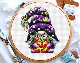 Può includere: Uno schema di punto croce di un gnomo che indossa un cappello viola e nero che tiene una zucca di Halloween. Lo gnomo è circondato da uno sfondo bianco.