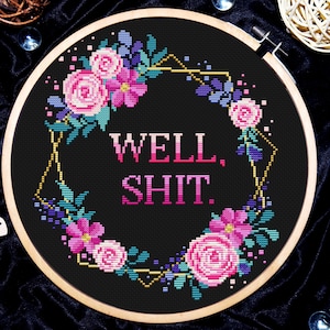 May include: A black embroidery hoop with a floral design and the text "WELL, SHIT." in pink letters.