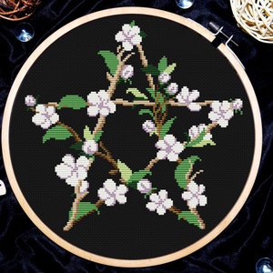 May include: A white pentagram with a floral design, featuring white flowers and green leaves, on a black background.