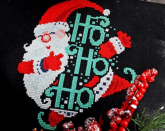 Może przedstawiać: Wzór haftu krzyżykowego przedstawiający kreskówkowego Świętego Mikołaja z napisem "Ho Ho Ho" w kolorze turkusowym i białym na czarnym tle.