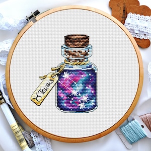 May include: A glass bottle filled with a purple and pink galaxy-like liquid with a cork stopper and a tag that says "Taurus".