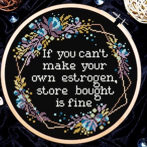 May include: Embroidered hoop art with a black background and floral border. The text reads "If you can't make your own estrogen, store bought is fine."