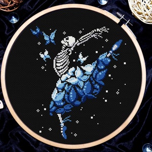 May include: A cross-stitch embroidery design of a skeleton ballerina in a blue and white tutu, surrounded by butterflies on a black background.