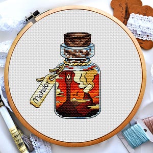 May include: A cross-stitch pattern of a glass bottle with a cork stopper. The bottle is filled with a dark liquid and has a label that reads "Mordor".