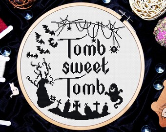 May include: Black and white cross-stitch embroidery hoop with the text "Tomb sweet Tomb" and Halloween imagery including bats, ghosts, and tombstones.