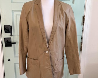 May include: A tan blazer with a single-button closure and two front pockets. The jacket is displayed on a white mannequin against a light green door background. The blazer has a classic lapel design.