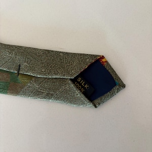 May include: A silk tie with a paisley pattern in shades of green and gold. The tie's interior is navy blue with a label that reads "SILK 100%."