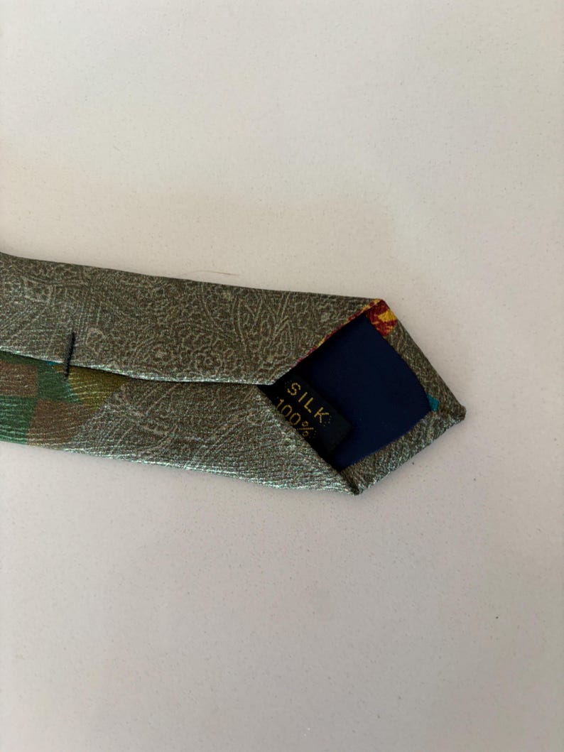 May include: A silk tie with a paisley pattern in shades of green and gold. The tie's interior is navy blue with a label that reads "SILK 100%."