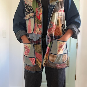 May include: A patchwork jacket with denim sleeves and a collar. The jacket features a variety of fabric patches in floral, plaid, and solid patterns. It has two front pockets and a button closure. The sleeves are rolled up.