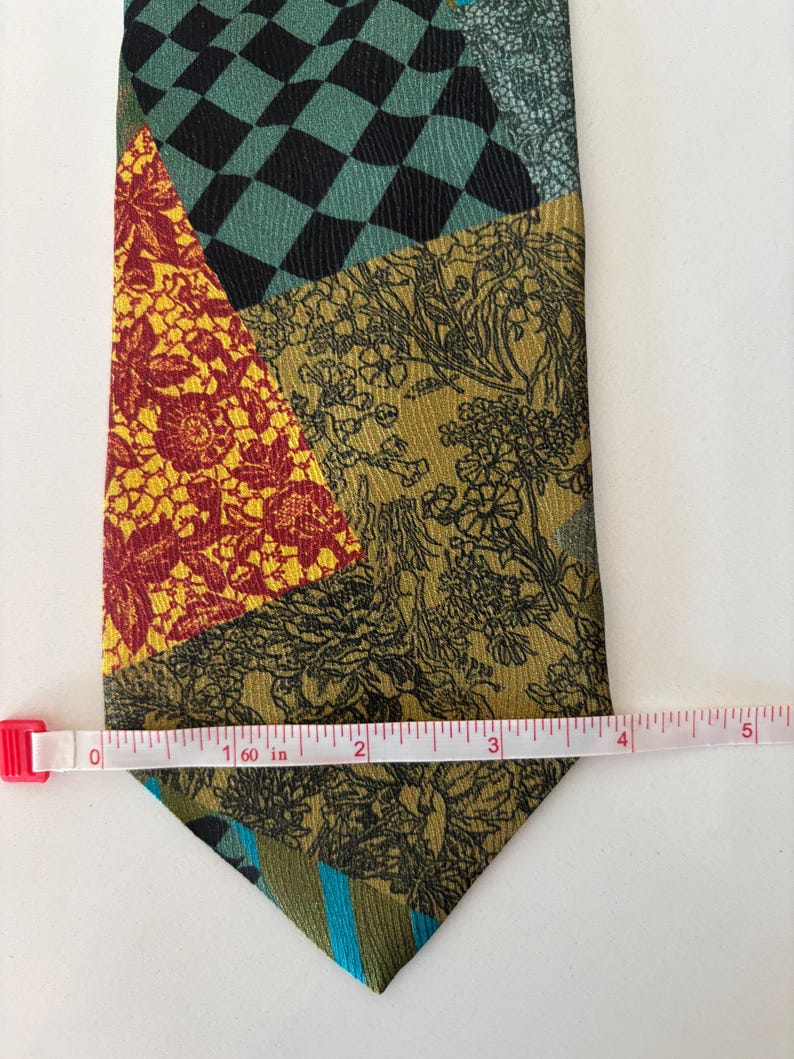 May include: A patchwork tie with various patterns and colors. The tie features sections of black and teal checkerboard, floral designs, and stripes. The tie is approximately 5 inches long.