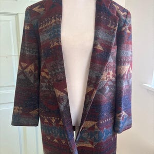 May include: A patterned blazer in shades of burgundy, blue, and tan. The open-front jacket features a geometric design and is displayed on a mannequin. The blazer has long sleeves and a classic lapel.