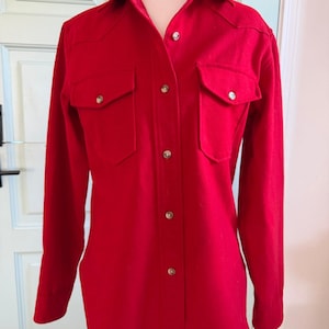 May include: A bright red button-down shirt with two chest pockets and silver-colored buttons. The long-sleeved shirt has a classic collar and a tailored fit. The shirt is displayed on a mannequin.