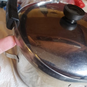 May include: A silver pot with a black handle and lid. The pot has a shiny surface and is slightly scratched.