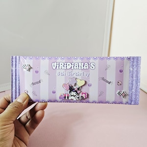 May include: A purple and white striped birthday card with the text "Viridiana's 8th Birthday". The card features cartoon characters, stars, skulls, and lightning bolts. The card is held by a hand.