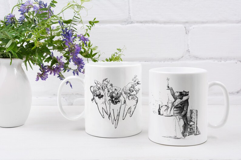 Op de afbeelding: Twee witte keramische mokken met zwart-wit illustraties. De ene mok heeft een groep cartoon tanden met gezichten en armen, terwijl de andere mok een cartoon dier in een pak laat zien dat een glas wijn vasthoudt.