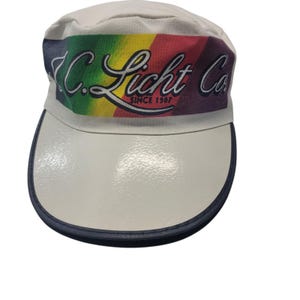 May include: White cap with a curved brim and a rainbow-colored band featuring the text "C. Licht Co. Since 1907." The brim is white with a navy blue trim. The cap is a vintage style.