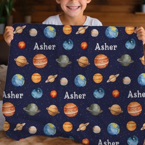 May include: A blue fleece blanket with a repeating pattern of planets and stars. The name "Asher" is printed on the blanket.