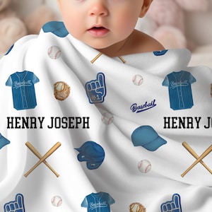 May include: White baby blanket with a baseball theme. The blanket features blue baseball jerseys, baseballs, baseball gloves, foam fingers, baseball bats, and baseball caps. The name "HENRY JOSEPH" is printed in bold black letters.