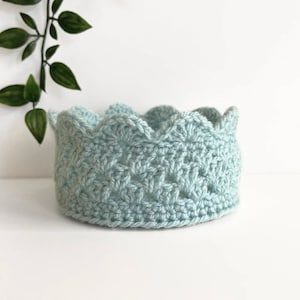 May include: A light blue crocheted crown with a scalloped edge.