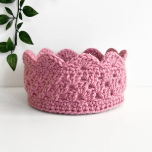 May include: A pink crocheted crown with a scalloped edge.