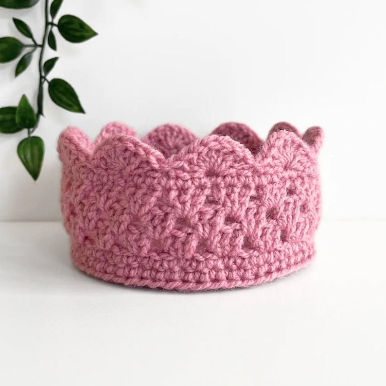 May include: A pink crocheted crown with a scalloped edge.