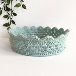 May include: A light blue crocheted crown shaped basket with a scalloped edge.