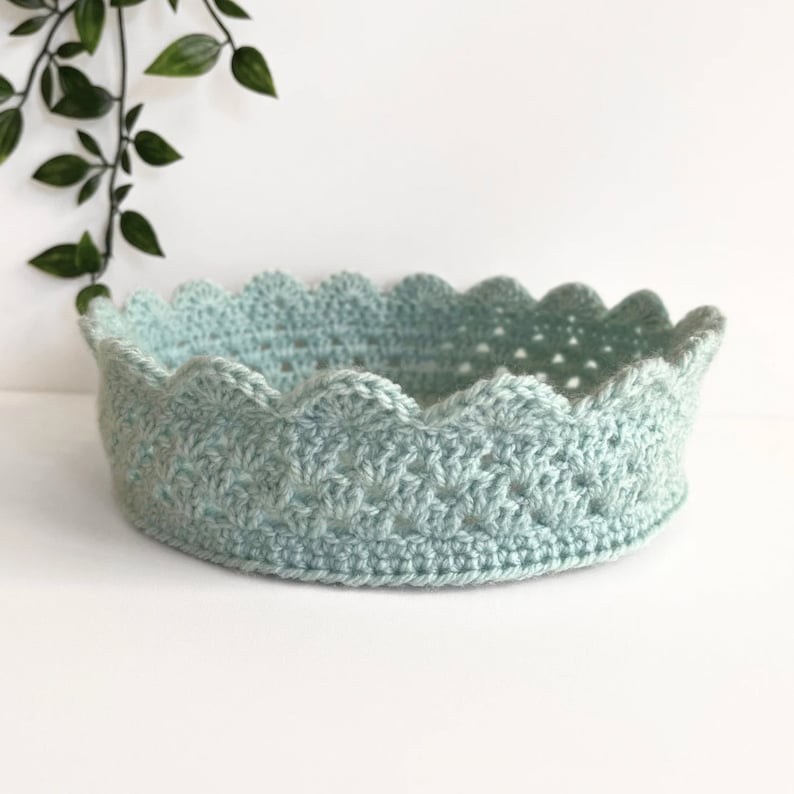 May include: A light blue crocheted crown shaped basket with a scalloped edge.