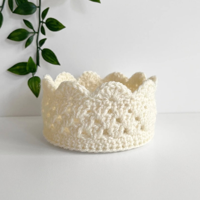 May include: A white crocheted crown with a scalloped edge. The crown is made with a delicate stitch pattern.