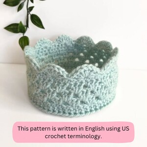 May include: A light blue crocheted crown with a scalloped edge. This pattern is written in English using US crochet terminology.