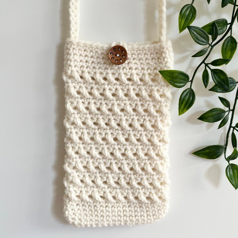 May include: A white crocheted crossbody bag with a wooden button closure. The bag has a simple, geometric design and is perfect for carrying small essentials.