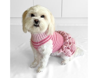 May include: A small white dog wearing a pink crocheted dress with a ruffled skirt.
