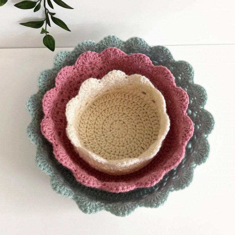 May include: Three crocheted bowls, nested together. The largest bowl is teal, the middle bowl is pink, and the smallest bowl is cream.