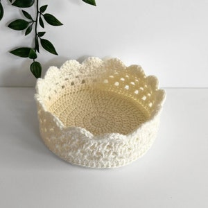 May include: A white crocheted basket with a scalloped edge. The basket is round and has a delicate, lacy design.