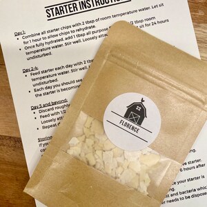Puede incluir: Una bolsa de papel marr&oacute;n con una ventana transparente que contiene virutas de iniciaci&oacute;n, y una pegatina blanca con un gr&aacute;fico de granero y la palabra "FLORENCE". Una hoja impresa de instrucciones titulada "STARTER INSTRUCTIONS" est&aacute; en el fondo.