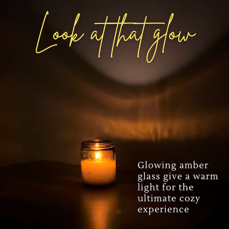 May include: A lit candle in a glass jar. The candle's flame casts a warm glow, with the text "Look at that glow" in cursive script at the top. The text "Glowing amber glass give a warm light for the ultimate cozy experience" is on the right.