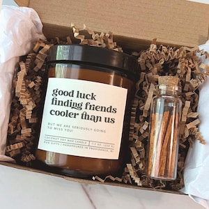 May include: A gift box containing a brown glass jar candle with a black lid and a small glass vial of matches. The candle label reads "good luck finding friends cooler than us." The candle is 7.5 oz (220 g). The box is filled with brown crinkle paper.