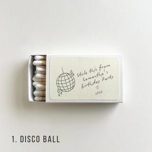 Pu&ograve; includere: Una scatola di fiammiferi bianca con un'etichetta color crema. L'etichetta presenta un'illustrazione di una palla da discoteca e un testo scritto a mano: "Stole this from Samantha's Birthday Party" con un cuore e l'anno 2026.