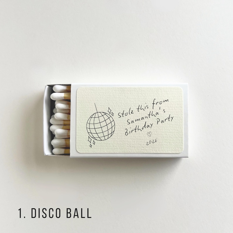 Pu&ograve; includere: Una scatola di fiammiferi bianca con un'etichetta color crema. L'etichetta presenta un'illustrazione di una palla da discoteca e un testo scritto a mano: "Stole this from Samantha's Birthday Party" con un cuore e l'anno 2026.