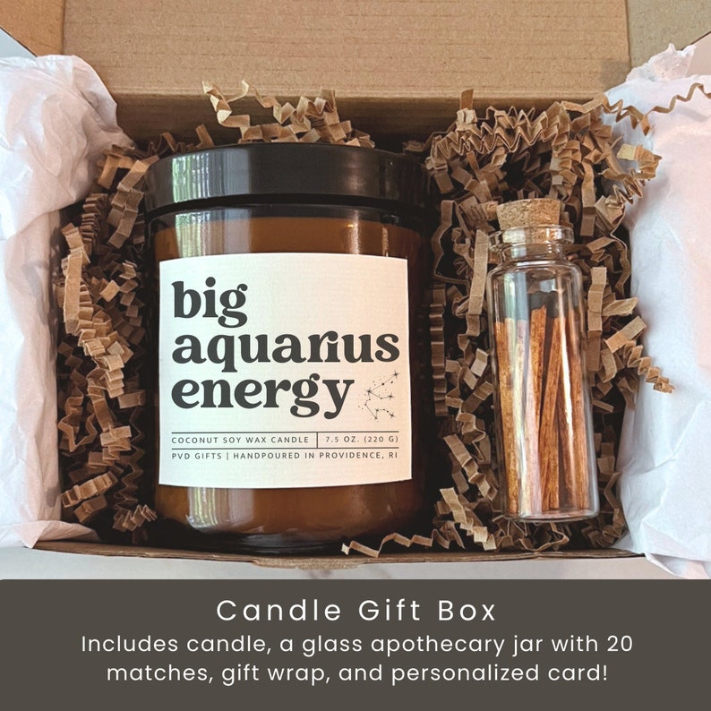 May include: A candle gift box with a large brown glass jar candle labeled "big aquarius energy." The box includes a small glass jar of matches, gift wrap, and a personalized card. The candle is 7.5 oz (220 g) and made with coconut soy wax.