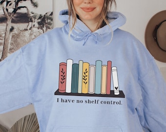 Puede incluir: Sudadera con capucha azul claro con un gráfico de una estantería llena de libros coloridos y el texto "I have no shelf control."