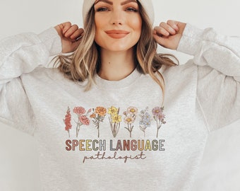 May include: A light gray sweatshirt with a floral design and the text "SPEECH LANGUAGE pathologist" in rainbow colors.