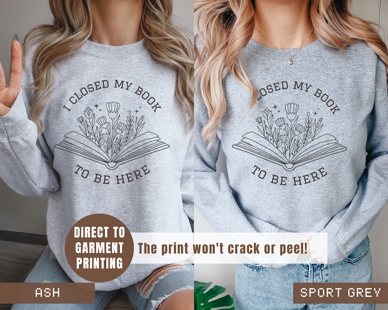 K&ouml;nnte beinhalten: Zwei graue Sweatshirts mit dem Text "Ich habe mein Buch geschlossen, um hier zu sein" darauf gedruckt. Der Text ist umgeben von einer Zeichnung eines offenen Buches, aus dem Blumen wachsen. Die Sweatshirts werden auf Models gezeigt, die Jeans tragen. Der Text "Direktdruck auf Kleidung" ist unten links im Bild gedruckt. Der Text "Der Druck rei&szlig;t nicht und l&ouml;st sich nicht ab!" ist unten rechts im Bild gedruckt. Der Text "Ash" ist unten links im Bild gedruckt. Der Text "Sport Grey" ist unten rechts im Bild gedruckt.