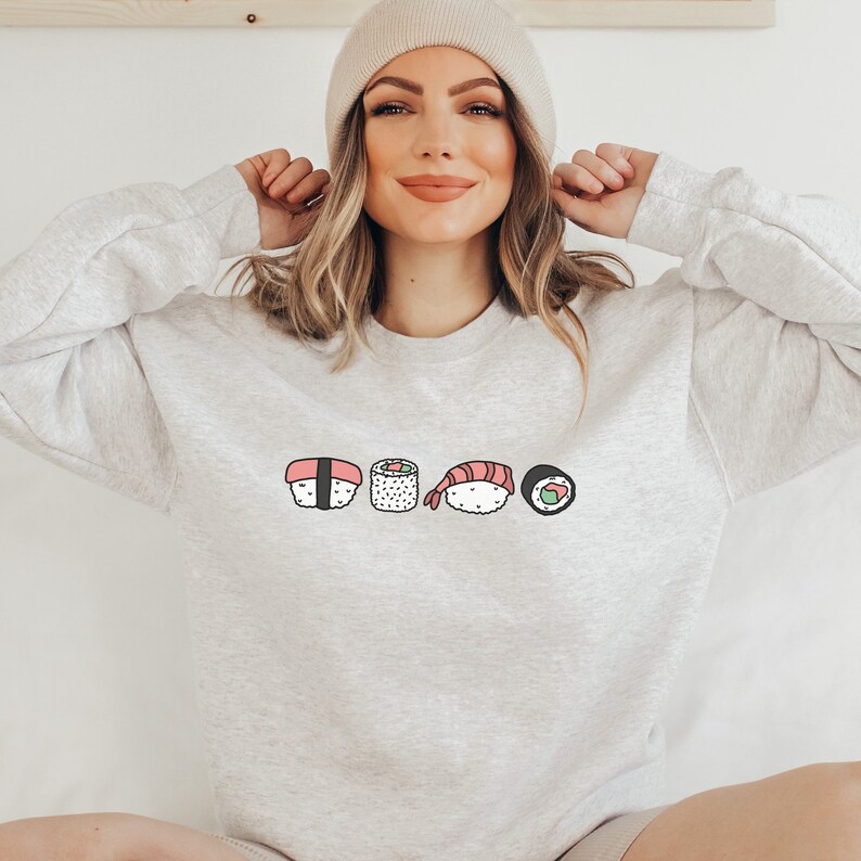 May include: A gray sweatshirt with a graphic of five different sushi rolls. The rolls are drawn in a cartoon style with pink, green, and black accents.