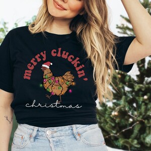 May include: A black t-shirt with a red and white illustration of a chicken wearing a Santa hat and Christmas lights. The text "merry cluckin' christmas" is printed on the shirt.