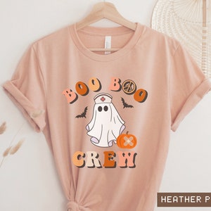 May include: A peach colored t-shirt with a graphic of a ghost wearing a nurse's hat and holding a pumpkin. The text "BOO BOO CREW" is above the ghost.