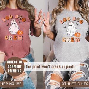 May include: Two t-shirts with a ghost wearing a nurse's hat and a pumpkin with a bandage. The text on the shirts reads "Boo Boo Crew". The shirt on the left is heather mauve and the shirt on the right is athletic heather.