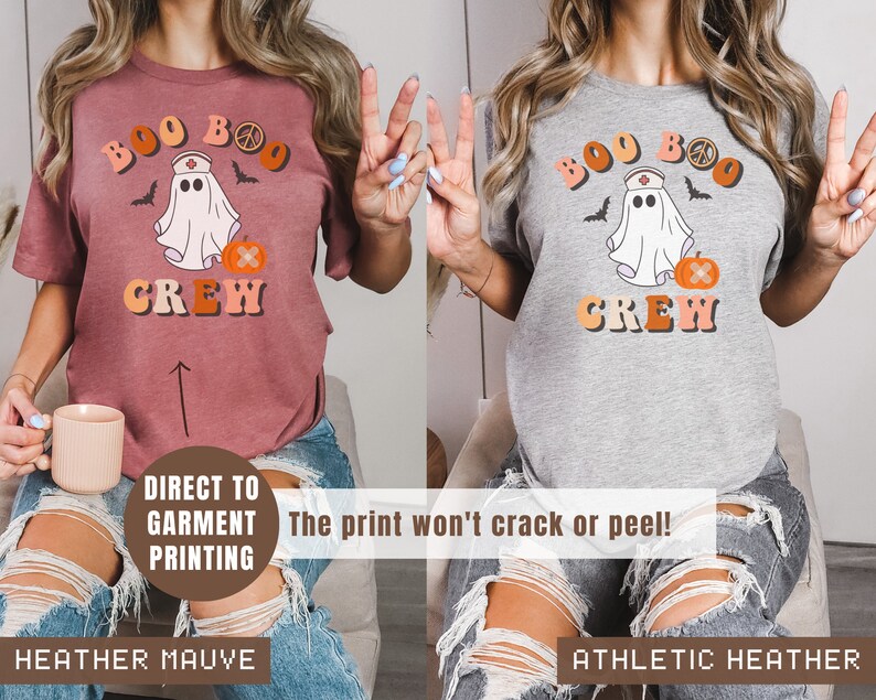 May include: Two t-shirts with a ghost wearing a nurse's hat and a pumpkin with a bandage. The text on the shirts reads "Boo Boo Crew". The shirt on the left is heather mauve and the shirt on the right is athletic heather.